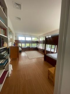 A room with multiple bunk beds and a bookshelf. Hardwood floors and a window with natural light.