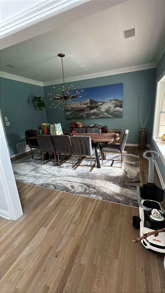 Dining room with wooden table, chairs, and rug. Teal walls with large artwork.
