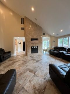 Spacious living room with a stone fireplace, leather couches, and tile flooring.
