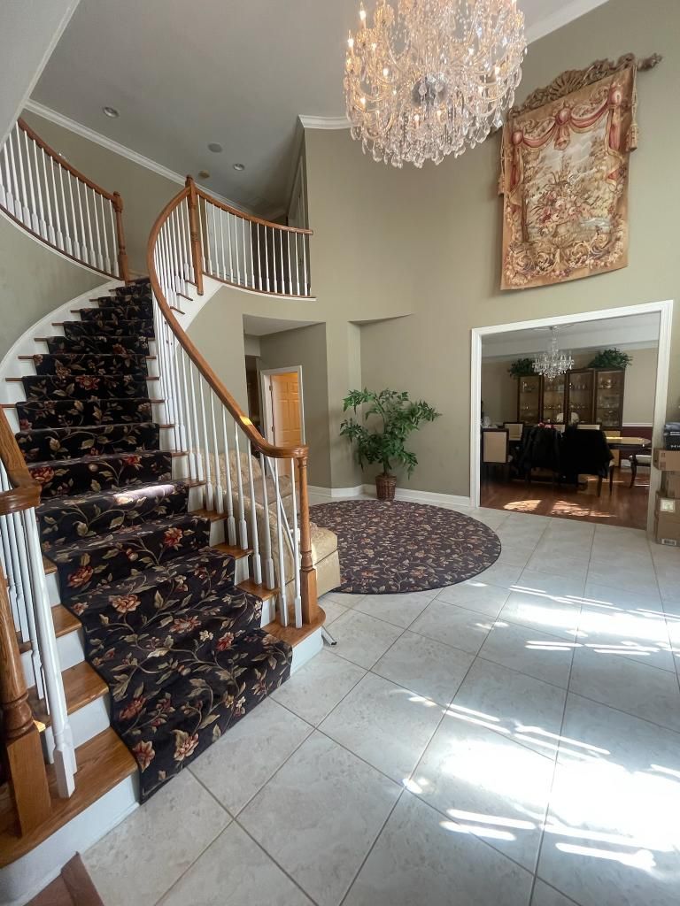 Grand entryway with a curved staircase, chandelier, tapestry, and tiled floor.