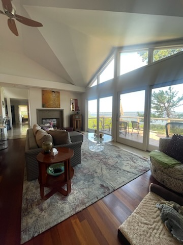 Living room with large windows overlooking water, vaulted ceiling, and hardwood floors.