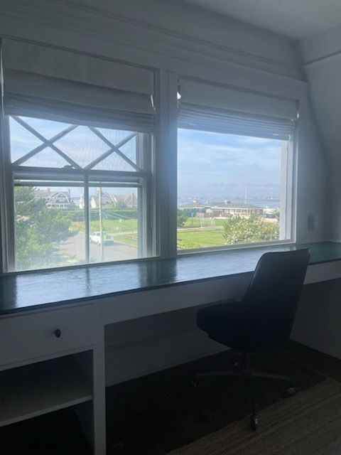 Desk with chair in front of windows, overlooking a park and water; bright daytime.