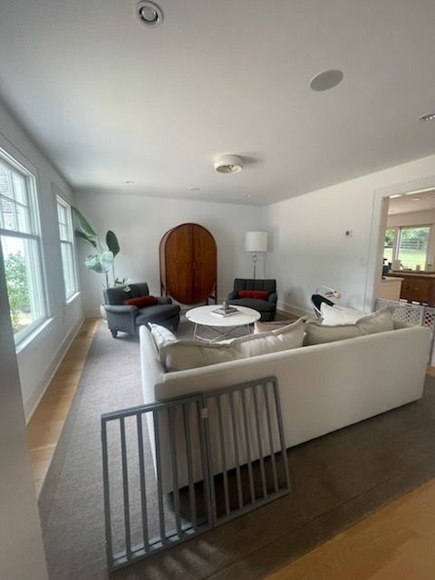 Living room with a white couch, two armchairs, and a wooden cabinet. A baby gate is in the foreground.