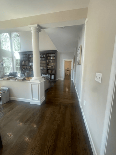 Dark wood-floored hallway with light walls, a column, and a bookshelf.