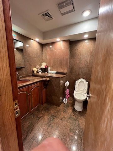 Small bathroom with brown tiled walls and floor. Wooden vanity and toilet are visible.