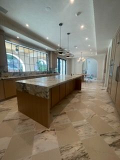 Large modern kitchen with marble counters and floors; wood cabinets, pendant lights.