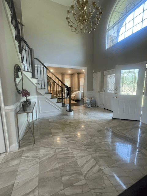 Spacious entry hall with marble floors, grand staircase, and chandelier.  Neutral tones, bright natural light.