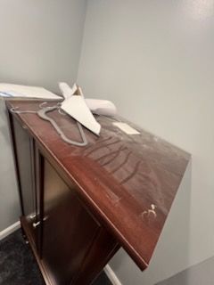 Wooden desk against a wall. Papers and debris are on top. Dark wood cabinet.