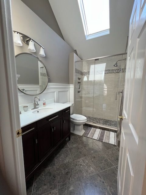 Bathroom with dark vanity, shower, toilet, and a skylight. Gray walls, dark floor, white trim.