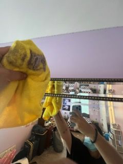 Person cleaning a mirror with a yellow cloth. Purple wall in the background.