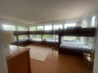 Bedroom with two bunk beds by large windows, wood floor, and dresser.