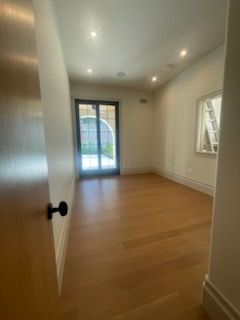Empty room with light wood floor, white walls, and a glass door leading to a garden.