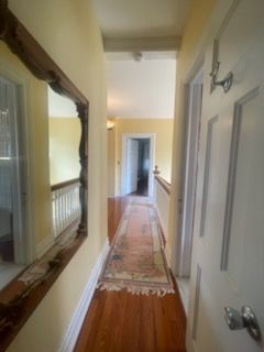 Hallway with wood floor, runner rug, yellow walls, and a large mirror.