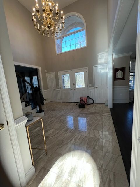 Spacious foyer with marble floors, double doors, chandelier, arched window, and vacuum cleaner.