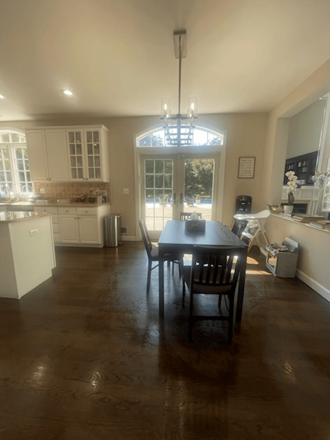 Kitchen with dark wood floor, dining table, white cabinets, French doors.