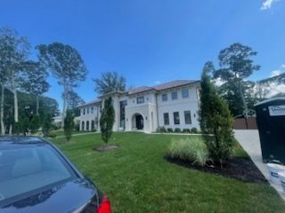 Large white house with green lawn, blue sky, car parked in front.