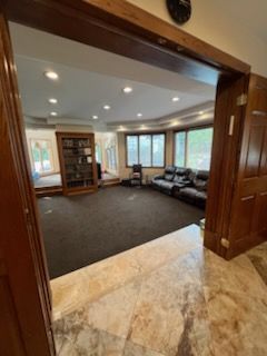 Living room with dark carpet, leather sofa, built-in bookcase, and large windows. Brown trim frames the doorway.