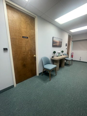Hallway with door, waiting area, teal chairs, beige desk, and a fire extinguisher.