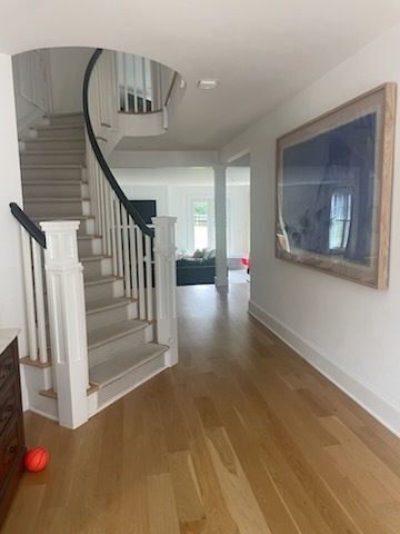 Entryway with stairs, hardwood floors, and a large framed artwork on a white wall.