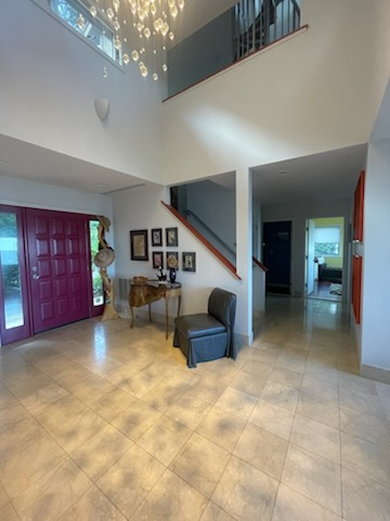 Spacious entry hall with burgundy door, staircase, and a small seating area.  High ceilings, neutral walls, and tile floor.