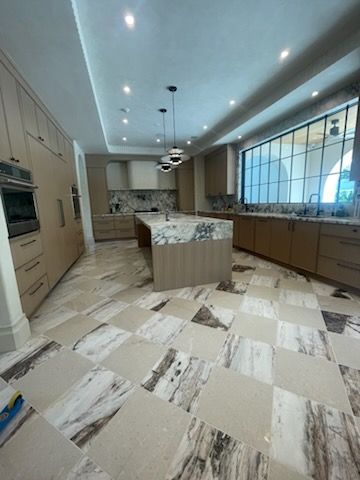 Spacious, modern kitchen with beige cabinets, marble countertops, checkered tile floor, and large windows.