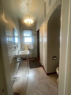 Narrow bathroom with pedestal sink, toilet, and archway, with tiled walls and a window.