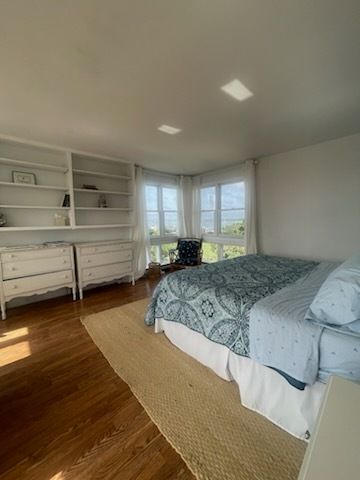 Bright bedroom with wood floors, white furniture, blue bedding, and a window seat.