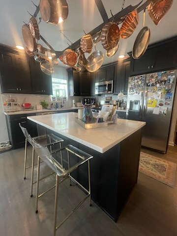 Kitchen with black cabinets, white countertop island, copper pots hanging from ceiling, and clear bar stools.