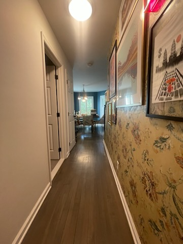 Narrow hallway with wooden floor, floral wallpaper, framed art, and a light fixture.