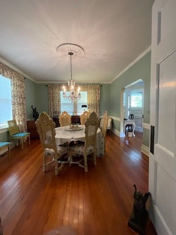 Formal dining room with round table, ornate chairs, and chandelier; hardwood floors and pale green walls.