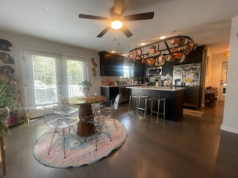 Open kitchen/dining area with dark cabinetry, a round wooden table with transparent chairs, and a unique light fixture.
