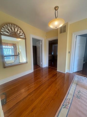 Hallway with hardwood floor, yellow walls, doorways, large mirror, and a hanging light.