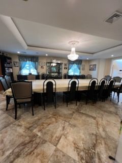 Long dining table with many chairs in a brightly lit room, tile flooring.