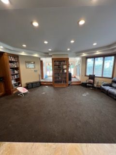 Spacious room with bookshelves, raised platform, and dark carpet. Beige walls, many recessed lights, and a sofa.