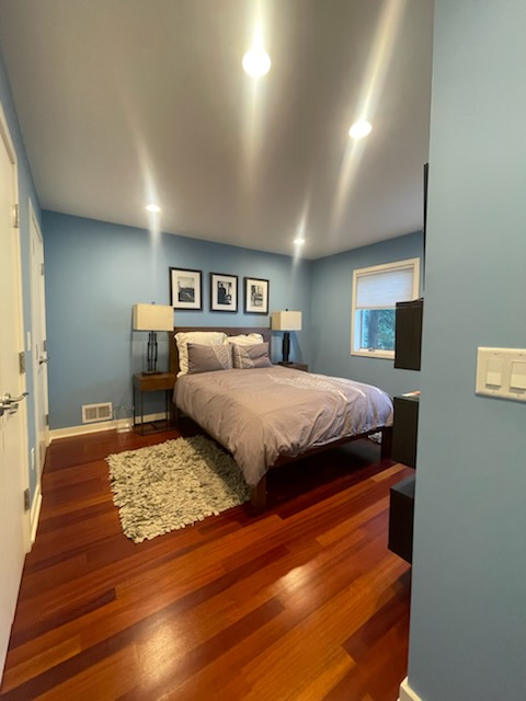 Bedroom with blue walls, hardwood floor, bed, and artwork.