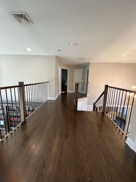Hallway with dark wood floor, railing, and a staircase. Neutral walls and white ceiling.