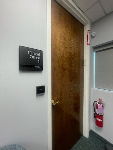 Door to a clinical office with a sign, fire extinguisher, and small window in a medical setting.