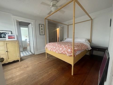 Bedroom with a yellow canopy bed, wood floors, and doorway leading to another room.