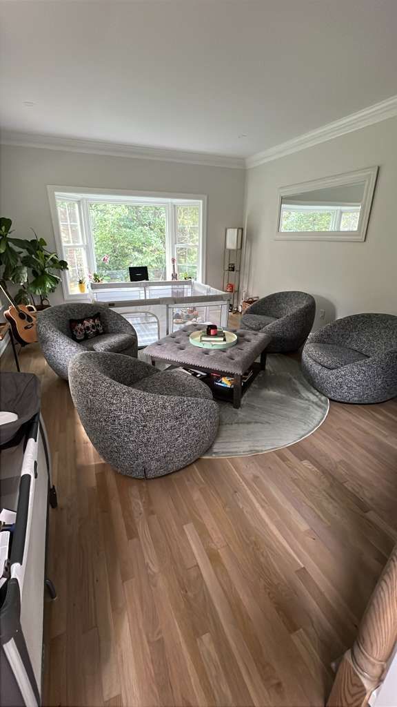 Living room with gray beanbag chairs, hardwood floors, and a center table. A large window and mirror are visible.