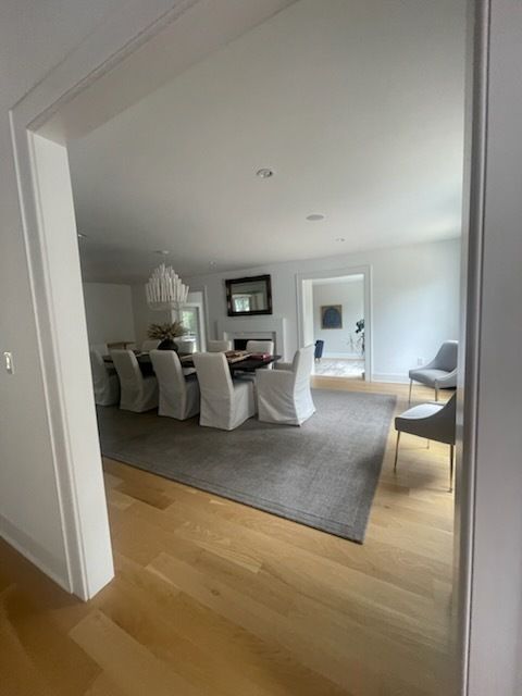 Dining room with a long table, white chairs, gray rug, and hardwood floors.