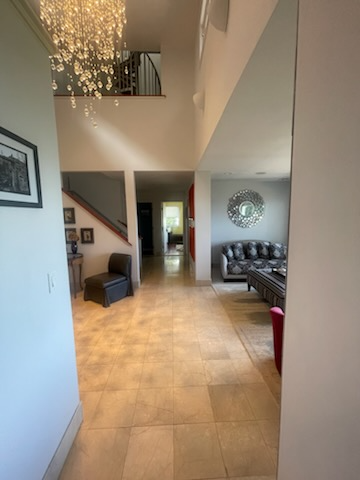 Interior view: Entryway with tile floor, stairs, chandelier, and living room with sofa and mirror.