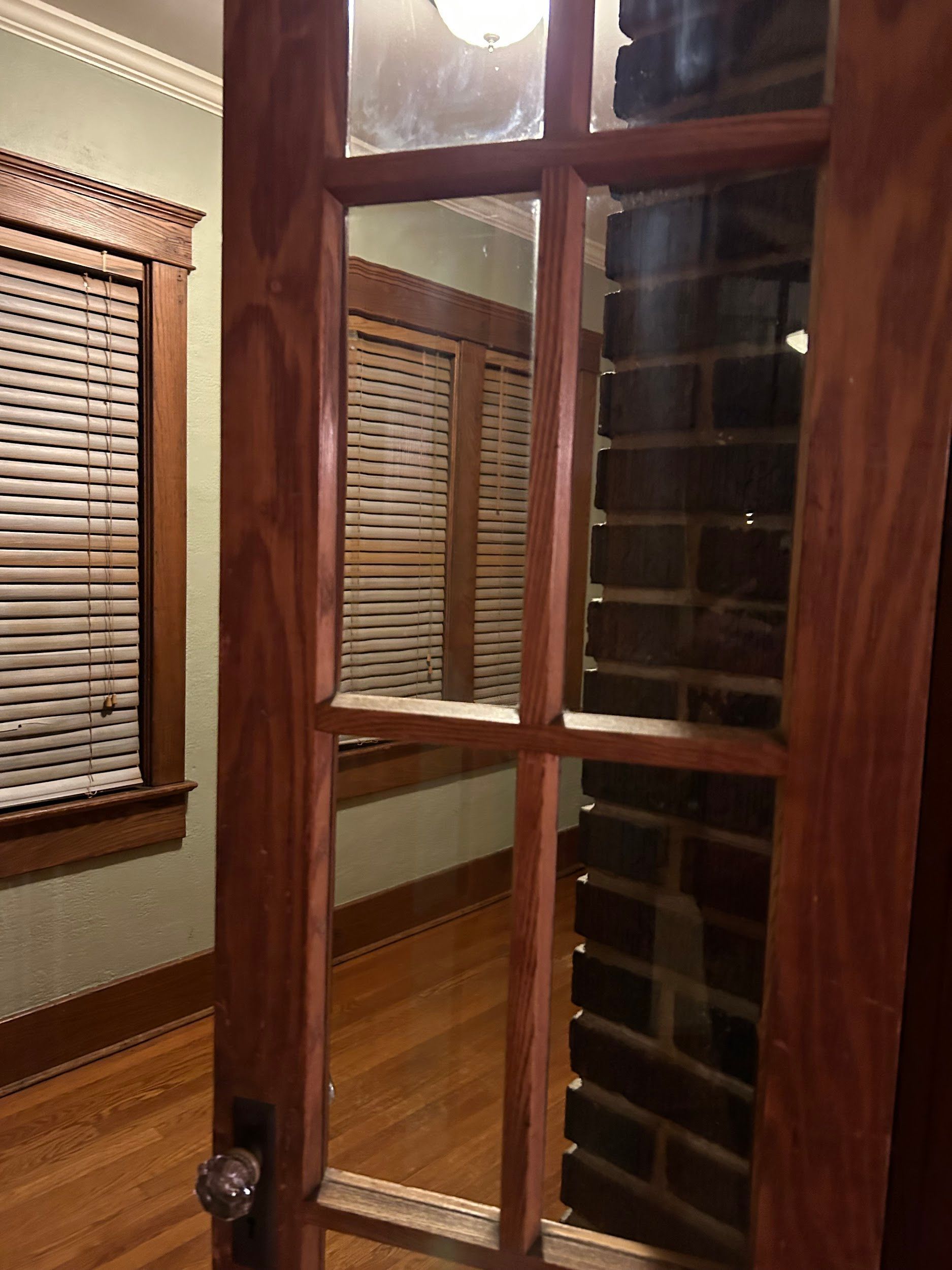 A wooden door is open to a room with blinds and a brick wall.
