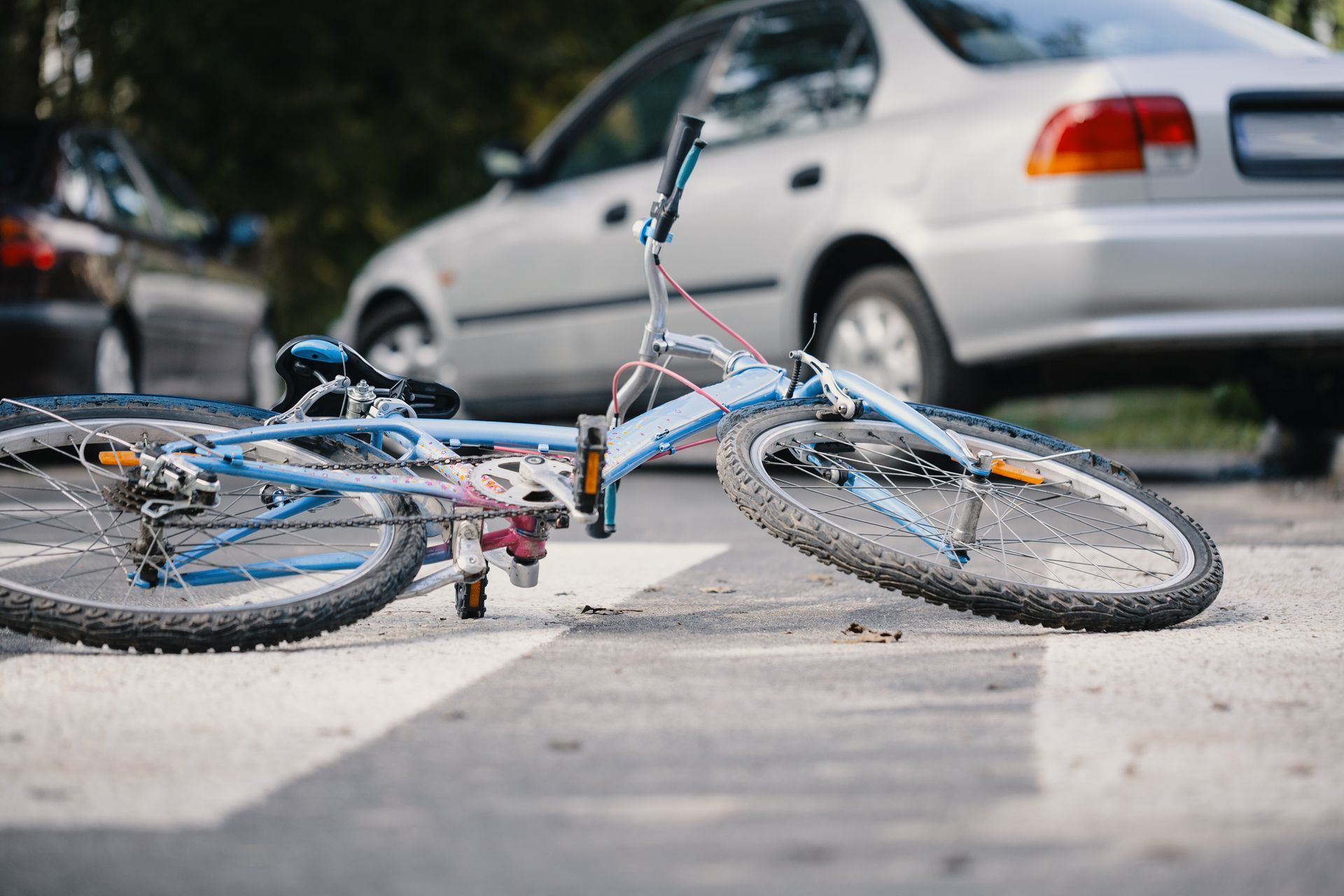 A bicycle lies on a crosswalk after a collision with a silver car.