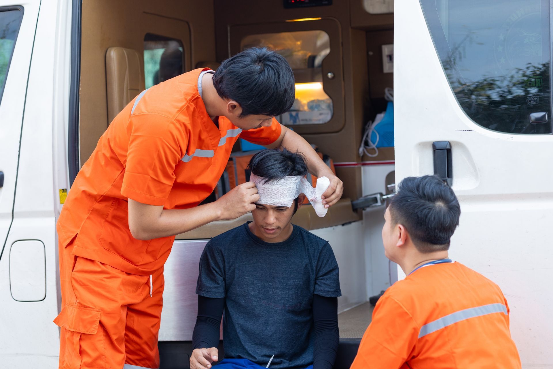Emergency medical technician bandaging a person's head inside an ambulance. Another technician assists.