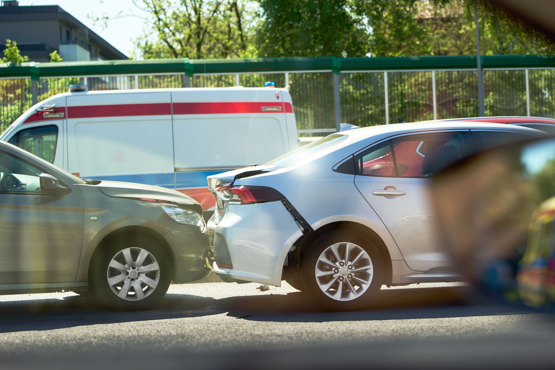 Cars involved in a rear-end collision on a road, with an ambulance in the background.