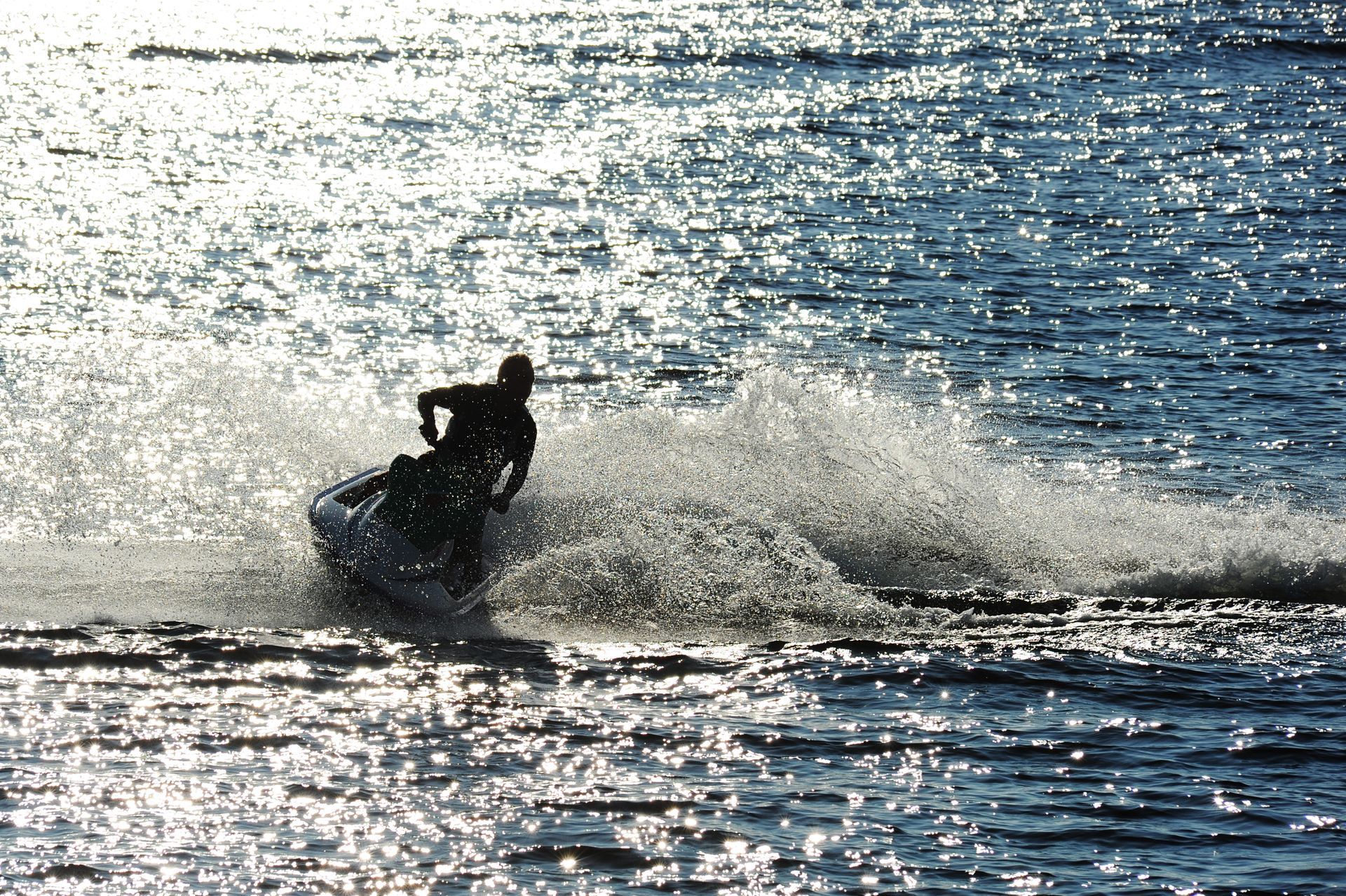 Jet skier on a lake, creating a large splash with the sun reflecting off the water.
