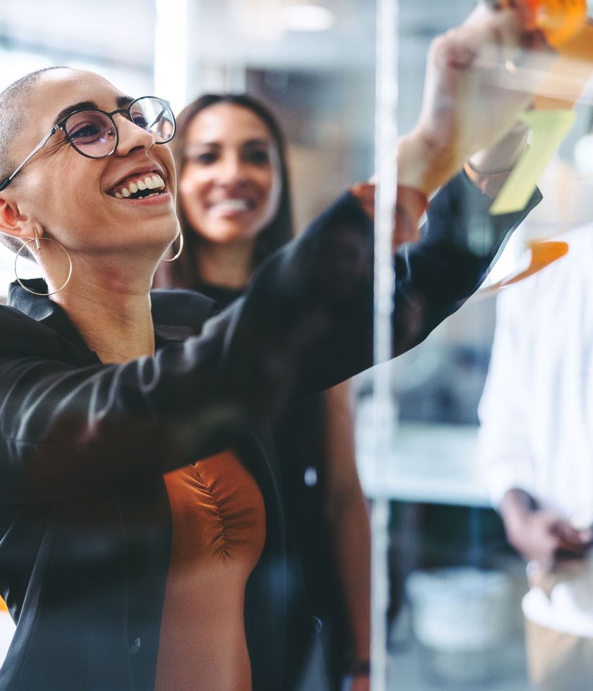 A woman wearing glasses is smiling while writing on a whiteboard.