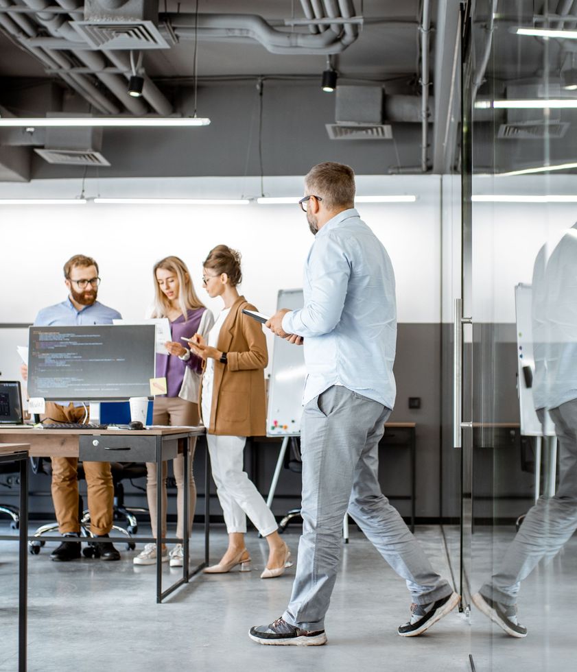 A man is walking through an office with a group of people sitting at desks.