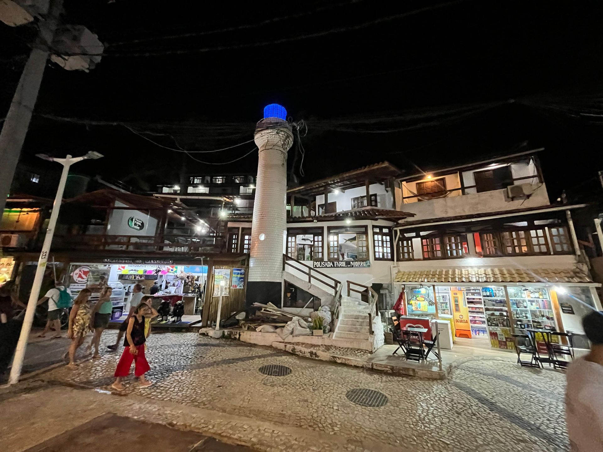 Um grupo de pessoas está caminhando em frente a um farol à noite.
