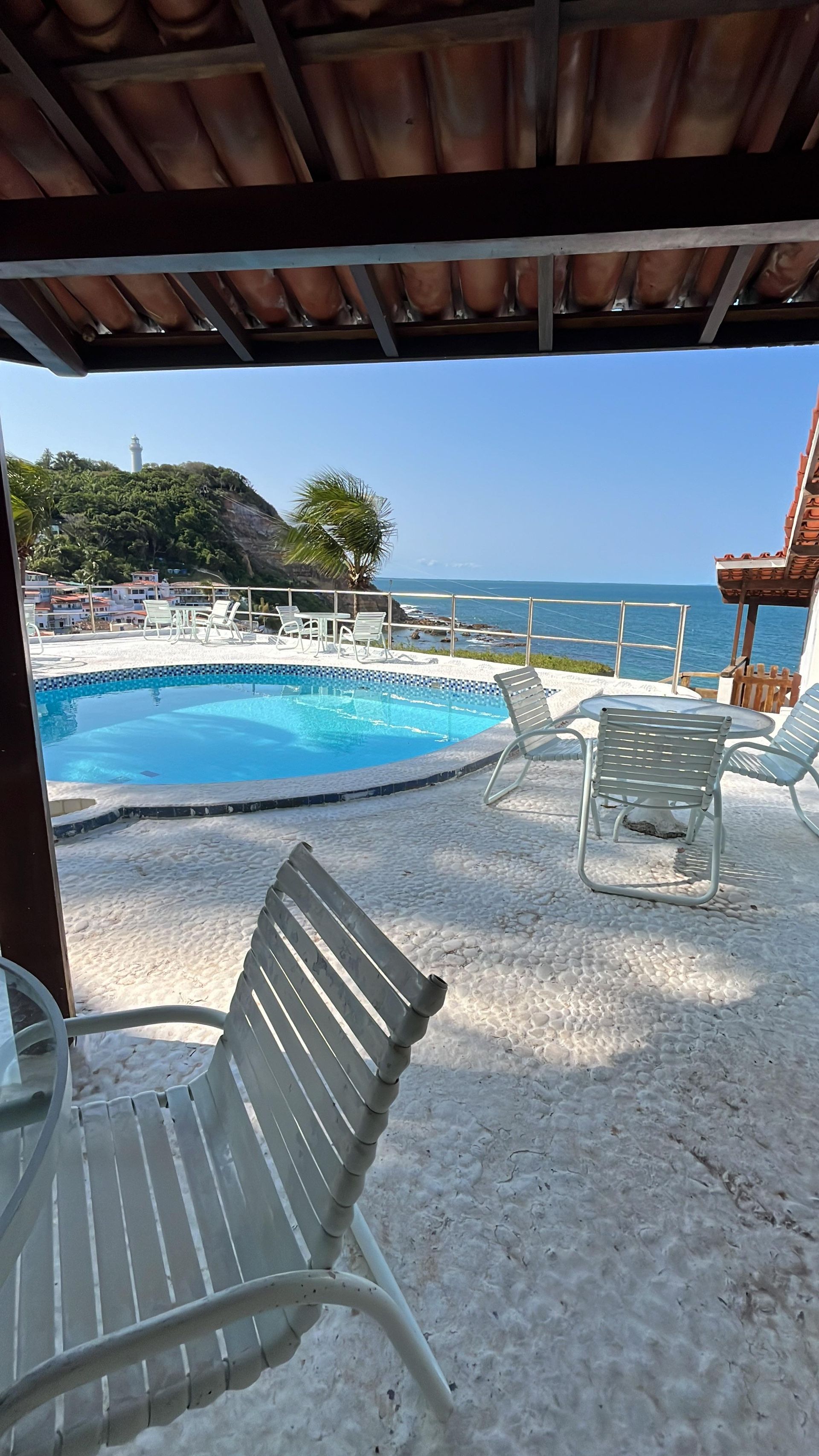 Há uma piscina ao fundo e uma mesa e cadeiras no primeiro plano.